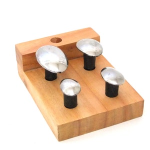 Puede incluir: Un juego de cuatro sellos de metal abovedados montados en una base de madera. Los sellos son de diferentes tamaños y se utilizan para crear impresiones decorativas en metal.