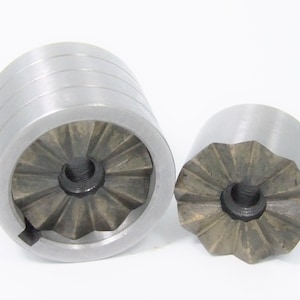 May include: Two metal tools with a star-shaped pattern and a center hole. The tool on the left is taller and has a smooth, cylindrical section.