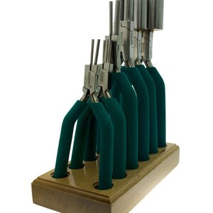 May include: A set of jewelry-making tools, including pliers and mandrels, displayed in a wooden holder. The pliers have green handles, and the mandrels are cylindrical. The tools are arranged vertically, showcasing their various sizes and shapes. The wooden holder has a light brown finish.