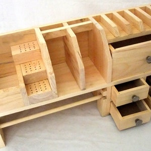 May include: A wooden organizer with multiple compartments, drawers, and shelves. The organizer is made of light wood and has a natural finish. It has a small shelf on top with slots for holding items. The organizer has three drawers on the bottom, one of which is open.