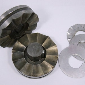 Puede incluir: Dos cortadores de galletas de metal con borde acanalado y un agujero central. Tres cortadores de galletas de metal adicionales con borde acanalado y un agujero central.