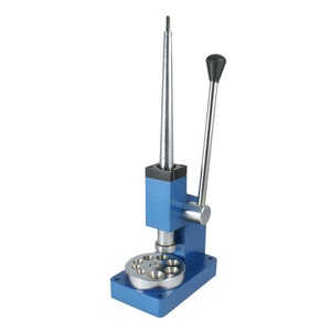 May include: A blue metal ring sizer with a metal mandrel and a lever handle. The sizer has a circular base with multiple ring sizing mandrels.