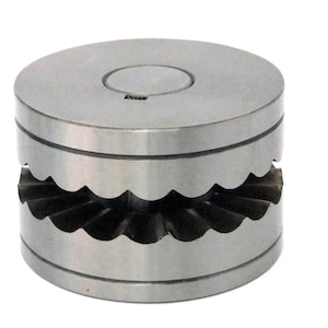 May include: A silver metal die with a scalloped edge and a small hole in the centre. The die is used for creating decorative edges on metal.