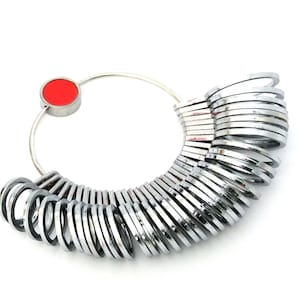 May include: A silver ring sizer with a red circle on the top. The sizer has a series of rings of different sizes.