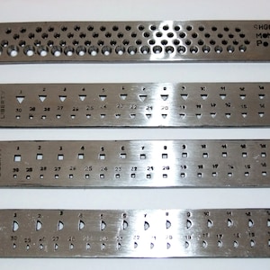 May include: Four metal rulers with different sized holes and markings. The rulers are labelled "LIBERTY" and have numbers from 14 to 30. The top ruler is labelled "32" and has a smaller hole pattern. The bottom ruler has a pattern of semi-circles. The top ruler also has the text "SHGM NOW POLY".