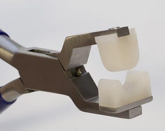 Könnte beinhalten: Metallzange mit silberfarbenem Finish und blauen Griffen. Die Backen sind mit zwei weißen, halbtransparenten, gebogenen Nyloneinsätzen ausgestattet, die dazu dienen, Gegenstände ohne Kratzer zu greifen, in geöffneter Position.