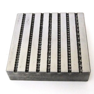 Puede incluir: Una placa de metal plateado con una serie de líneas paralelas grabadas en la superficie. Las líneas están espaciadas uniformemente y crean un patrón texturizado.