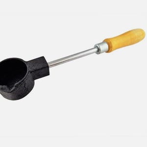 Op de afbeelding: Een zwarte metalen lepel met een ronde kom en een lange, zilveren steel. De steel heeft een houten handvat. Deze tool wordt waarschijnlijk gebruikt voor het smelten of gieten van materialen.