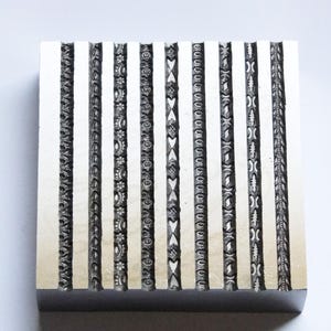 May include: A metal block with 12 different decorative patterns engraved into its surface. The patterns are all linear and appear to be for use in creating borders or trim.