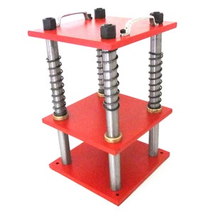 May include: A red wooden press with a square base and top, connected by metal rods and springs. The top has two silver handles and black nuts. The design suggests a mechanical or industrial tool.