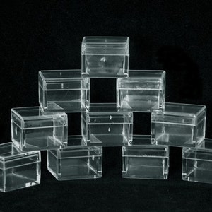 May include: A pyramid arrangement of clear, square plastic boxes with hinged lids. The transparent boxes allow a view of the contents. The boxes are stacked against a black backdrop.