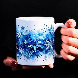May include: White ceramic mug with a blue and white snowflake design. The snowflakes are scattered across the mug and appear to be painted in a watercolor style.