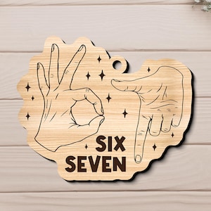 May include: Wooden sign with a light brown finish, featuring hand gestures and the words "SIX SEVEN" in a bold, dark brown font. The design includes star accents and a small hole for hanging.