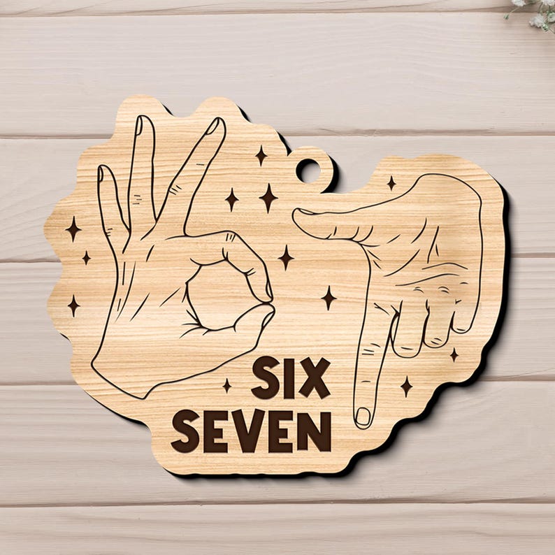 May include: Wooden sign with a light brown finish, featuring hand gestures and the words "SIX SEVEN" in a bold, dark brown font. The design includes star accents and a small hole for hanging.