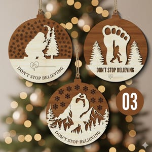 May include: Three wooden Bigfoot-themed Christmas ornaments. Each ornament features a different Bigfoot design, with the phrase "Don't Stop Believing" and a heart symbol. The ornaments are round with a natural wood grain finish and snowflake cutouts.