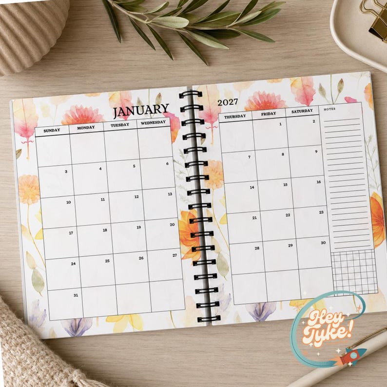 May include: A spiral-bound 2027 calendar open to the month of January. The pages feature a white grid layout with black text for days of the week and dates, decorated with watercolour-style orange, yellow, and pink floral illustrations.