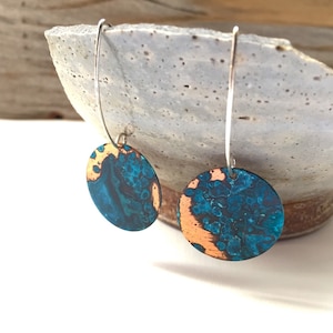 May include: A pair of dangle earrings with a round, teal and copper disc pendant on each earring.