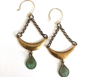 May include: A pair of gold earrings with a crescent moon shape and a teardrop-shaped pendant. The earrings are made of brass and have a vintage look.