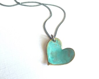 May include: A silver chain necklace with a turquoise heart pendant. The heart is made of metal and has a rustic, aged look.