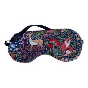 K&ouml;nnte beinhalten: Eine marineblaue Schlafmaske mit einem Waldmuster mit einem Hirsch, einem Fuchs, Pilzen und floralen Elementen. Die Maske hat einen schwarzen, verstellbaren Riemen. Das Design umfasst rosa, rote und gr&uuml;ne Akzente.