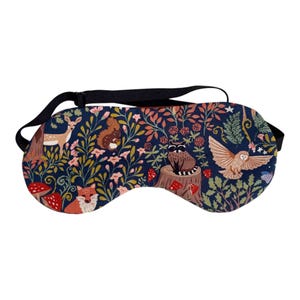 K&ouml;nnte beinhalten: Eine marineblaue Schlafmaske mit einem Waldmotiv, das ein Reh, ein Eichh&ouml;rnchen, einen Fuchs, eine Eule und einen Waschb&auml;ren zeigt. Die Maske hat ein schwarzes Gummiband und ist mit Blumen, Pilzen und Bl&auml;ttern verziert.