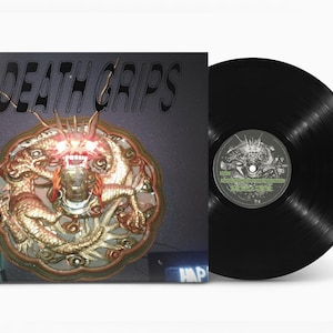 Pode incluir: Um álbum de vinil com o texto "DEATH GRIPS" na capa. A arte do álbum apresenta um design dourado e ornamentado com uma criatura semelhante a um dragão. O disco em si é preto.