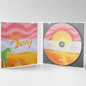 May include: A CD case open, revealing a disc and cover art. The cover art features the text "Bad Bunny" in yellow script over a desert landscape with a sunset. The CD itself has a similar design.