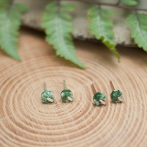 May include: Three pairs of green agate stud earrings with gold accents on a wooden surface.