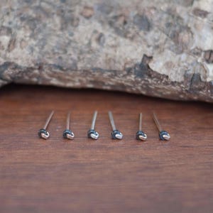 May include: Six silver nose rings with black beads on a wooden surface.