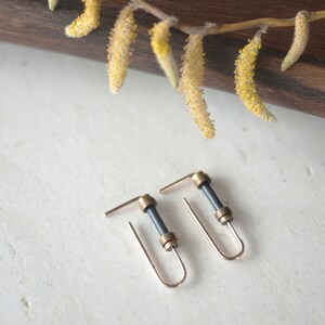 May include: A pair of gold hoop earrings with a black cylindrical accent. The earrings are on a white surface.