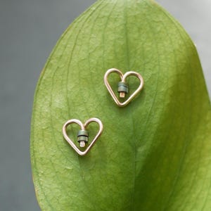 May include: A pair of gold heart-shaped earrings with a green and gold accent in the center of each heart.