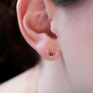 May include: Gold heart-shaped earrings with a small iridescent bead in the centre.