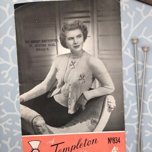May include: A black and white photo of a woman wearing a knitted cardigan with a floral design. The photo is from a vintage knitting pattern booklet. The text on the booklet reads "A Templeton Design N°834 4d".
