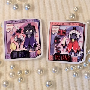 May include: Two illustrated character cards featuring a cartoon goat and lamb. The goat card is purple and says "Unholy Ally" and "The Goat". The lamb card is pink and says "Cult Leader" and "The Lamb".