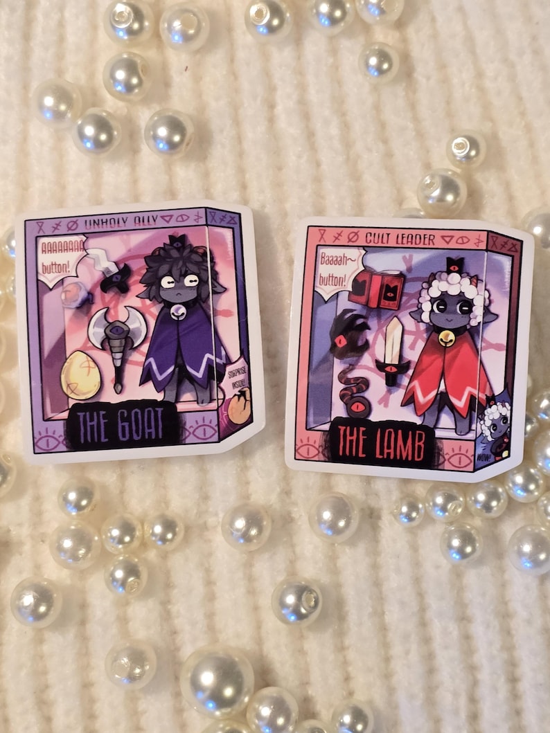 May include: Two illustrated character cards featuring a cartoon goat and lamb. The goat card is purple and says "Unholy Ally" and "The Goat". The lamb card is pink and says "Cult Leader" and "The Lamb".