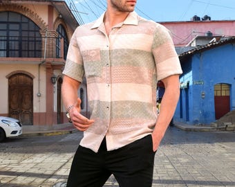 Op de afbeelding: Kort mouwshirt met een beige basis en horizontale strepen in groen en roze. Het shirt heeft een borstzak en een klassieke kraag. Het model draagt een zwarte broek.