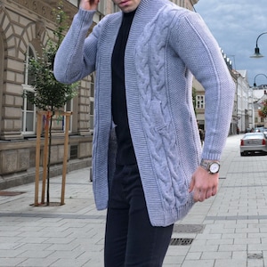 Könnte beinhalten: Ein hellgrauer Strickcardigan mit Stehkragen und langen Ärmeln. Der Cardigan hat eine lockere Passform und ist vorne offen.