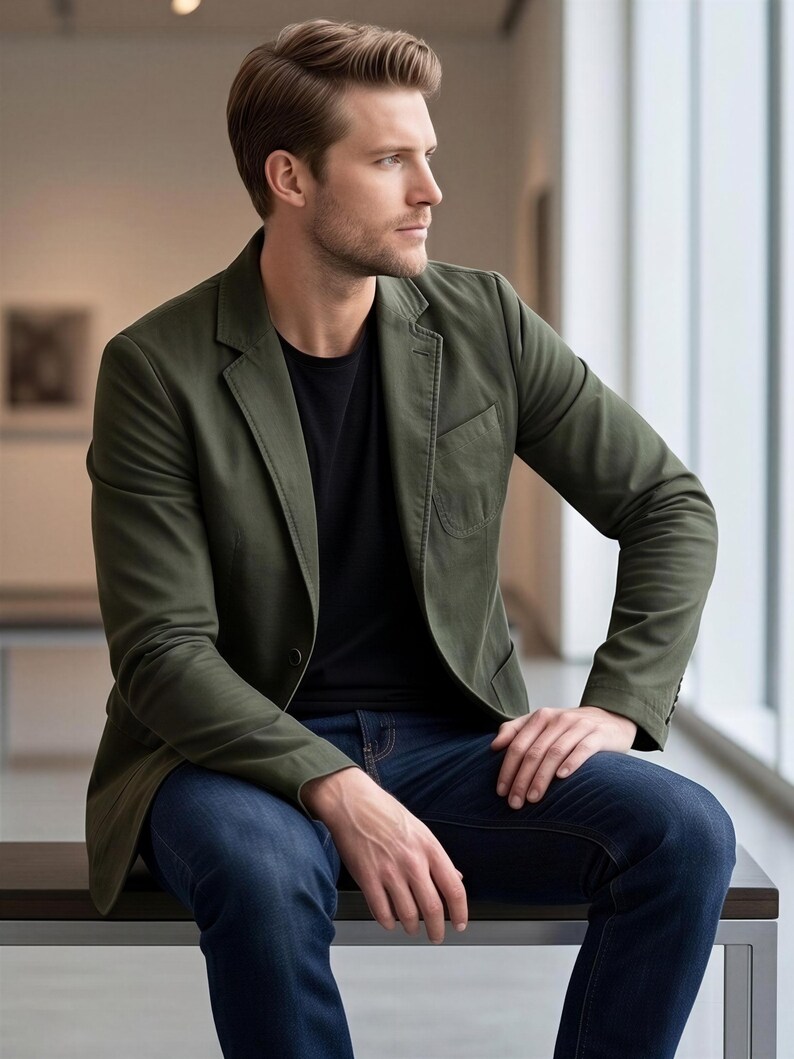 A man in a green blazer and blue jeans sits on a bench, looking off to the side with a thoughtful expression.