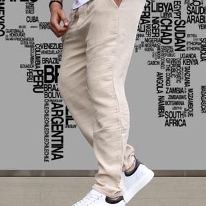 May include: Beige linen pants with a drawstring waist and side pockets. The pants are paired with white sneakers with black accents. The background features a world map design.