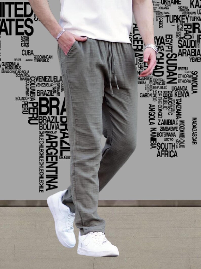 May include: Olive green linen pants with a drawstring waist and pockets. The pants are paired with white sneakers and a white t-shirt. The background features a world map graphic.