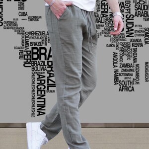 May include: A person wearing olive green drawstring pants and white sneakers. The person is also wearing a white t-shirt. The background features a world map design with country names in a gray color.