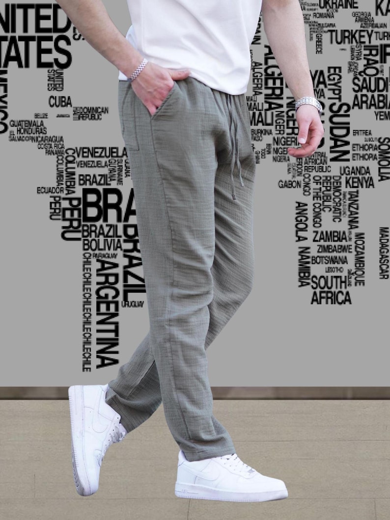 May include: A person wearing olive green drawstring pants and white sneakers. The person is also wearing a white t-shirt. The background features a world map design with country names in a gray color.