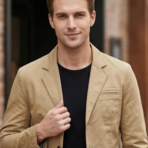A man wearing a tan blazer and black shirt is smiling and looking directly at the camera.