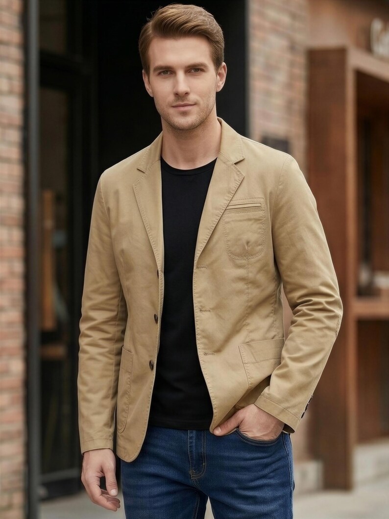 A man wearing a tan blazer and black shirt stands in front of a brick building.