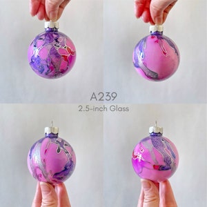 May include: A pink glass Christmas ornament with silver and purple marbling. The ornament is 2.5 inches in diameter. A239.