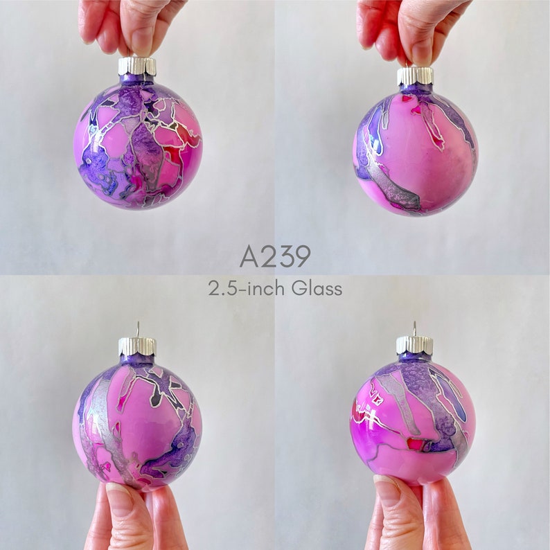 May include: A pink glass Christmas ornament with silver and purple marbling. The ornament is 2.5 inches in diameter. A239.