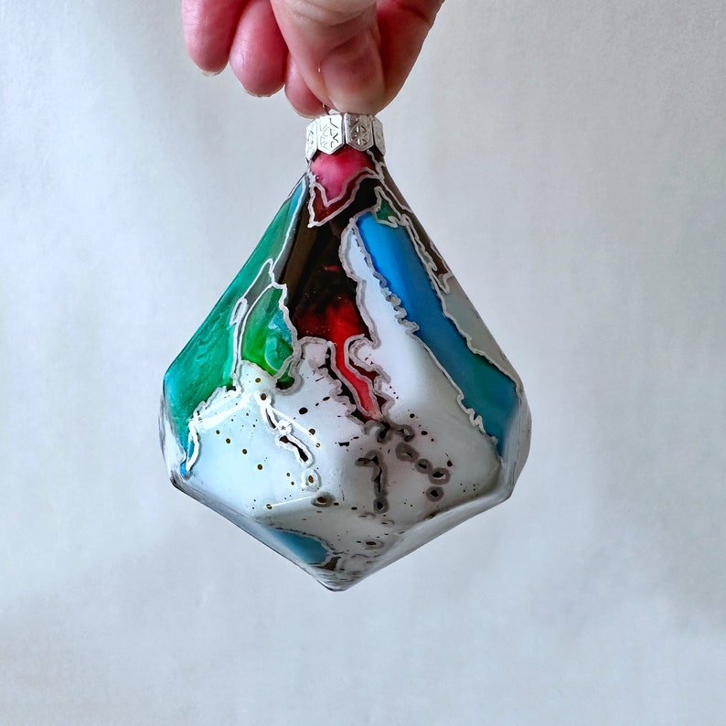 A diamond glass ornament that will stand out on your holiday tree. Filled with a rainbow of colors creating a unique pattern outlined in silver highlights. Created by Sarah John Afana for schemata on Etsy.