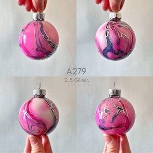 May include: A pink and purple glass Christmas ornament with silver swirls. The ornament is 2.5 inches in diameter. A279.