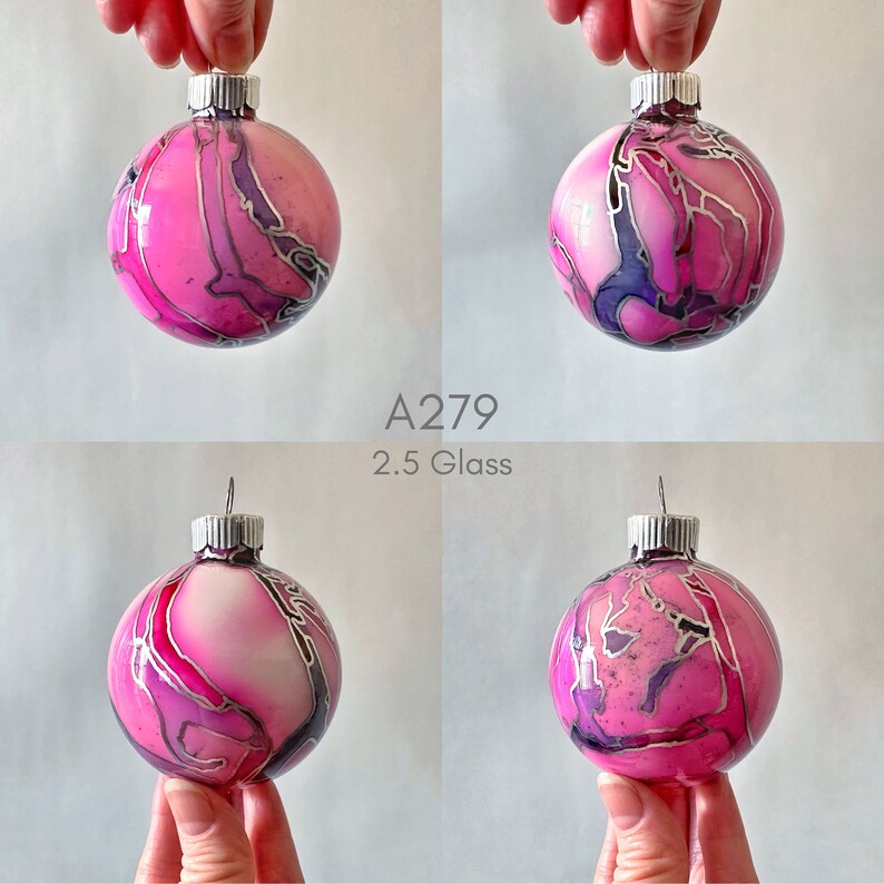 May include: A pink and purple glass Christmas ornament with silver swirls. The ornament is 2.5 inches in diameter. A279.
