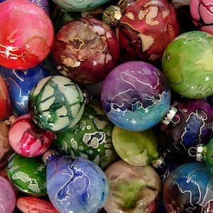 May include: A collection of colorful glass ornaments with intricate patterns and designs. The ornaments are a mix of round and teardrop shapes, and they are all decorated with swirls and lines of silver paint.